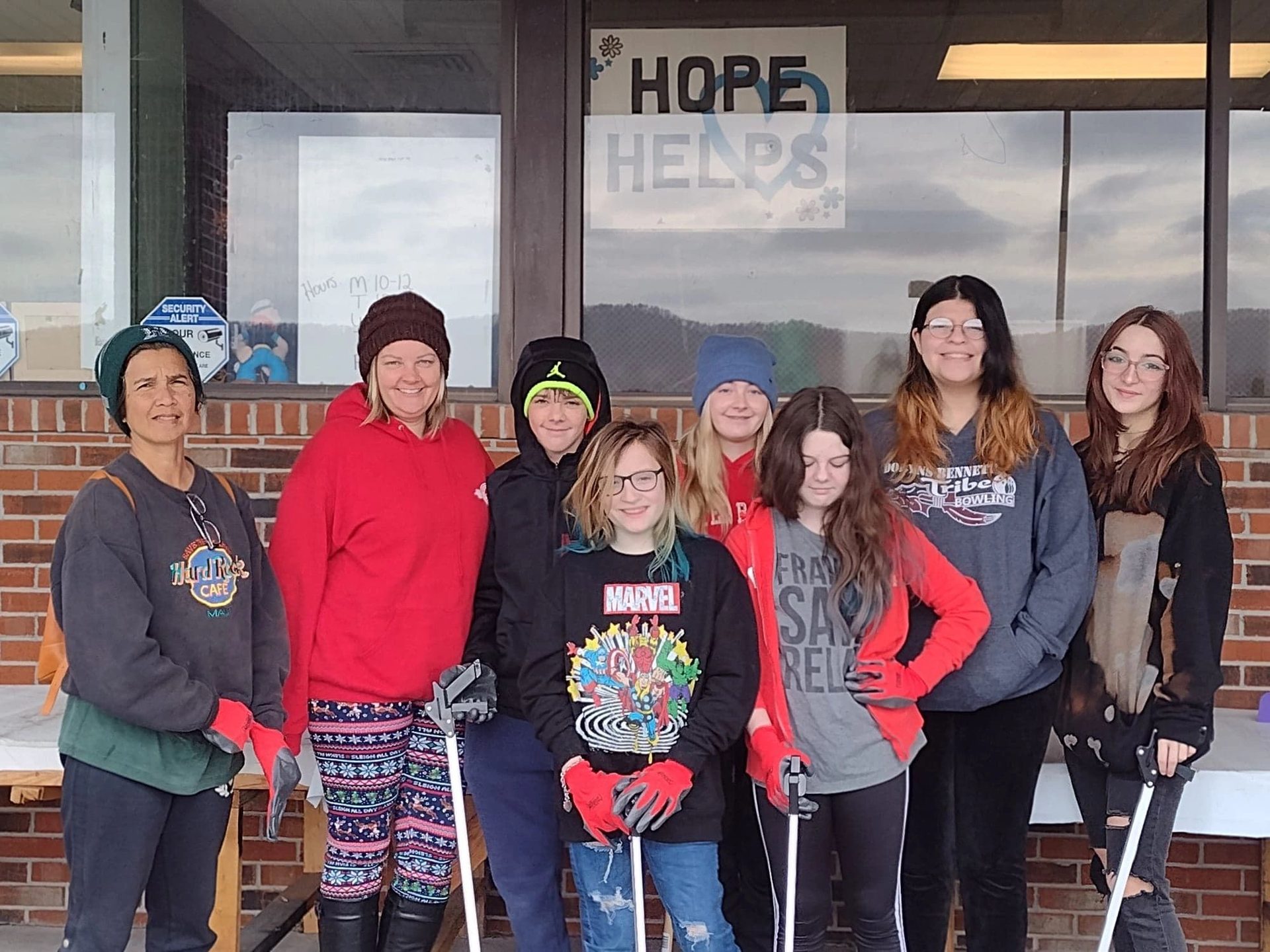 A group of young people in coats and gloves outside the pantry, under the hand-painted HOPE HELPS window sign
