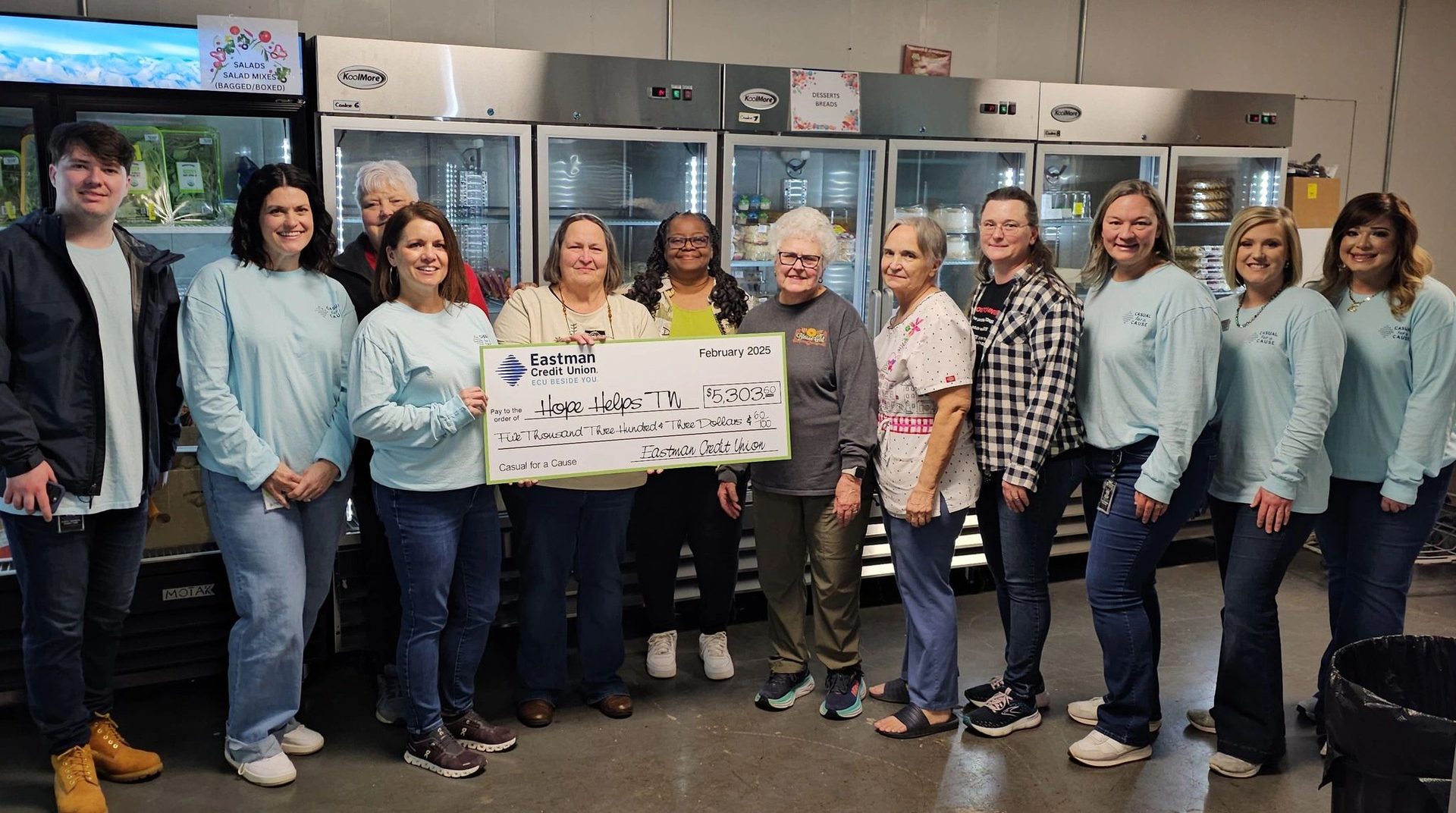 A group gathered in the pantry holding a large donation cheque from Eastman Credit Union