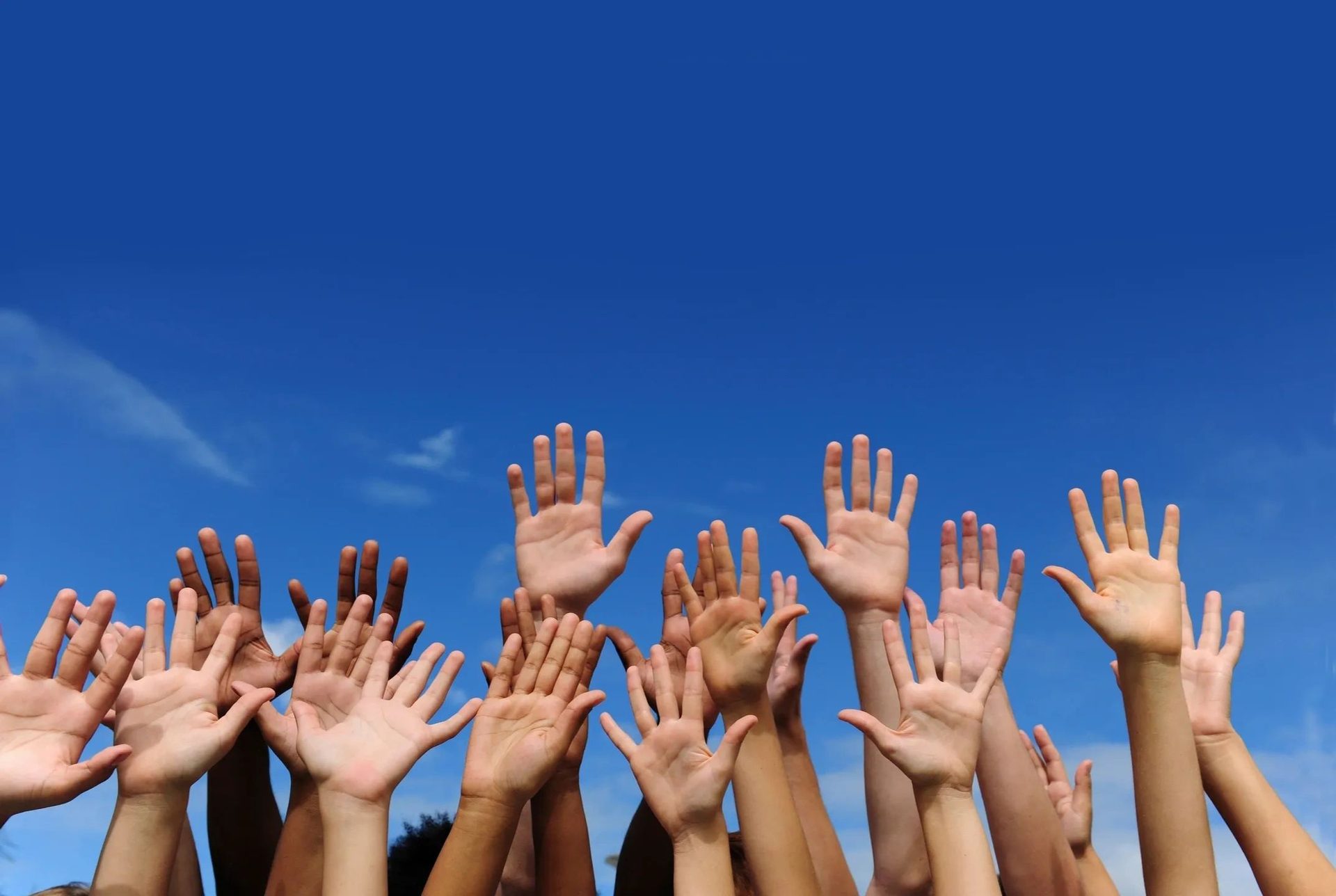 Many hands raised together against a blue sky