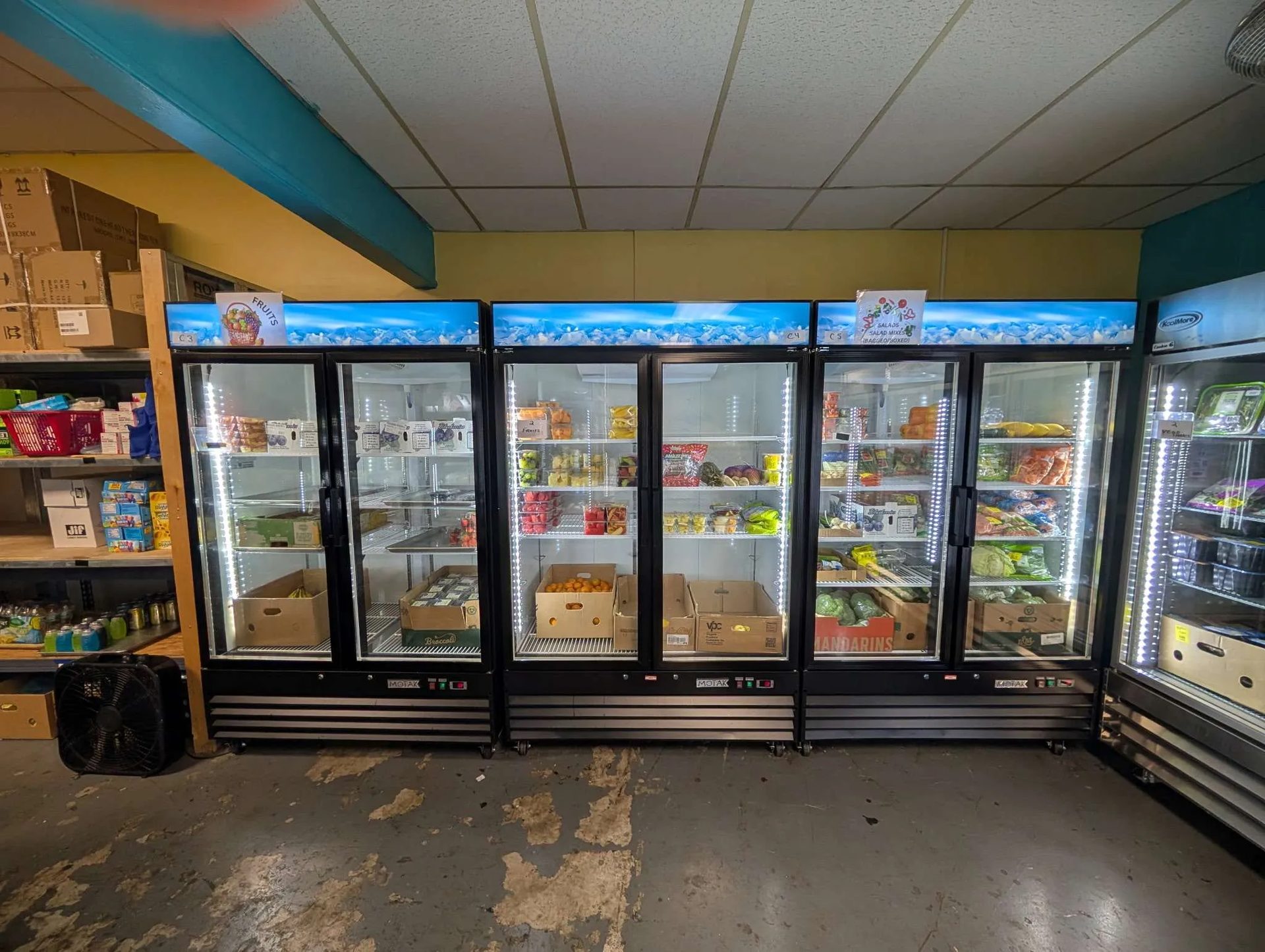 Glass-door coolers stocked with fresh fruit, labelled by shelf