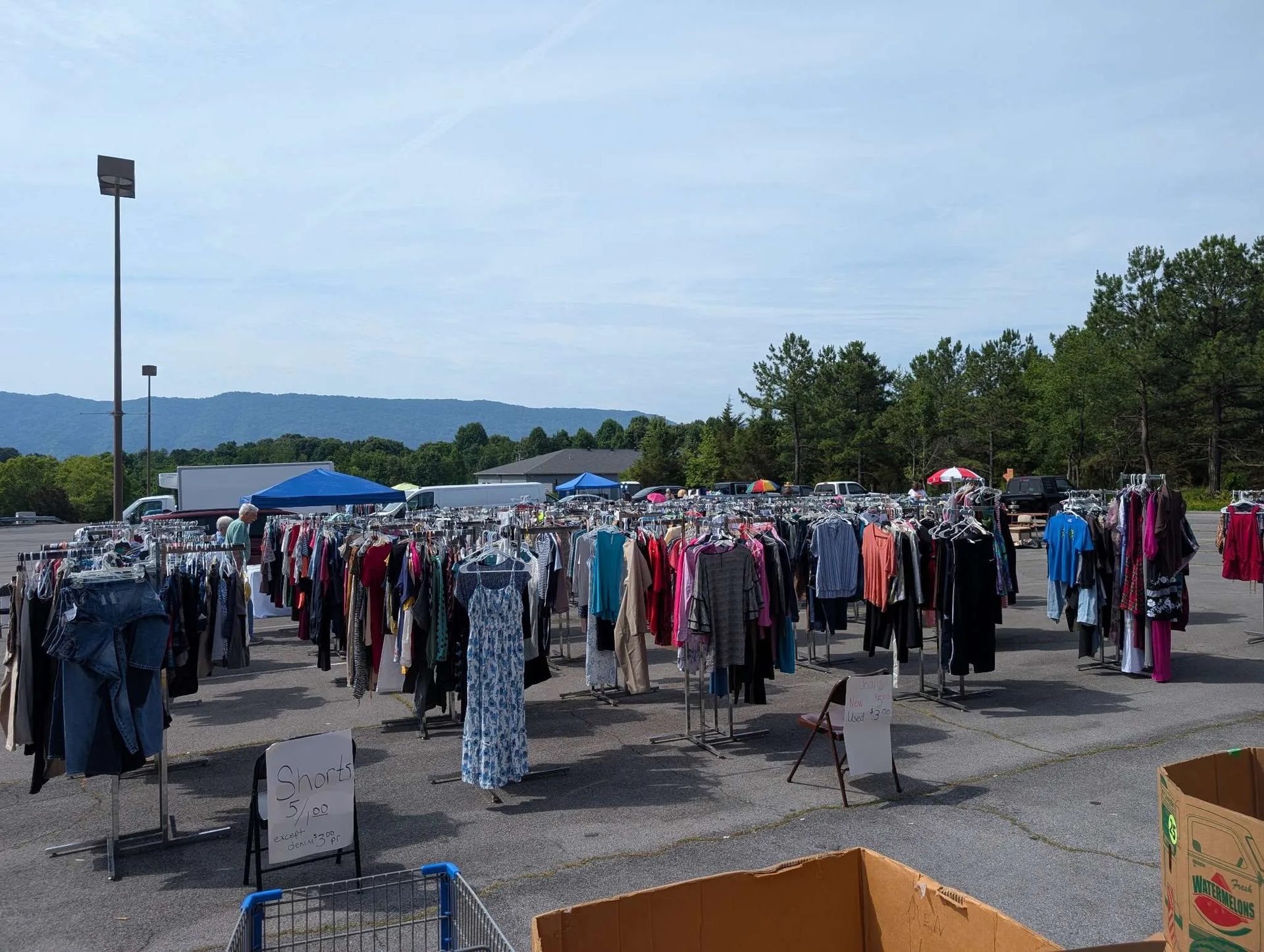 Rows of clothing racks set out across the car park on yard sale morning, mountains behind
